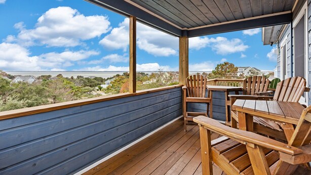 Eine überdachte Veranda mit Holzstühlen und einem Tisch, mit Blick auf eine malerische Landschaft mit Häusern und Bäumen.