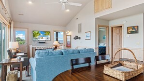 Ein geräumiges Wohnzimmer mit einem blauen Sofa, einem Holzessttisch und einem Deckenventilator.