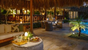 An outdoor lounge area with a thatched roof, wicker furniture, and a pool.