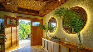 A spacious hallway with a wooden door leading to a balcony, a console table with plants, and a large mirror with a circular frame.
