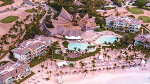 An aerial view of a resort with a large pool, multiple buildings, and a beachfront.