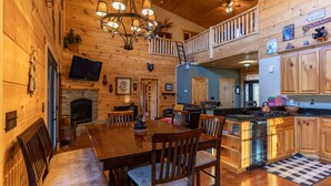 A cozy cabin interior with a dining area, kitchen, and a loft bedroom.