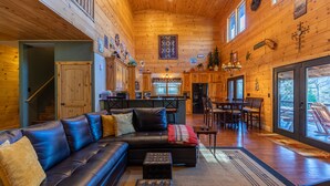 A spacious living area with a large black leather sectional sofa, a wooden dining table with chairs, and a kitchen area with a bar.