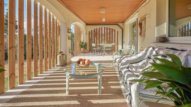 A covered outdoor area with a dining table and chairs, a wicker chair, and a sofa with patterned cushions. - Amazing home in Breda (Breda)