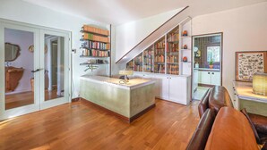 A spacious living area with a wooden floor, a central island with a lamp, a bookshelf, and a dining area with a leather couch. - Amazing home in Breda (Breda)