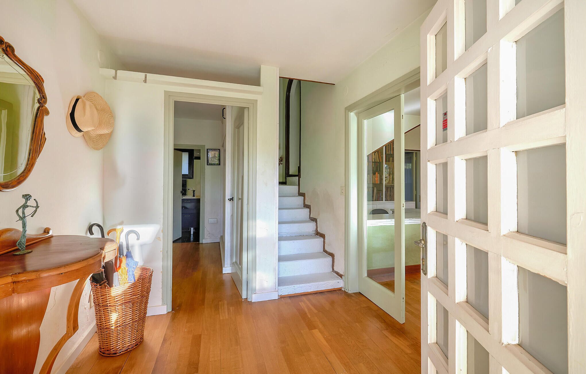 A hallway with a wooden floor, a mirror, a wicker basket, and a door leading to another room.