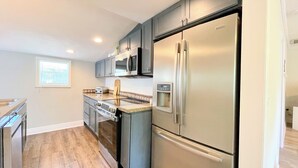 A modern kitchen with stainless steel appliances, grey cabinets, and a wooden countertop.