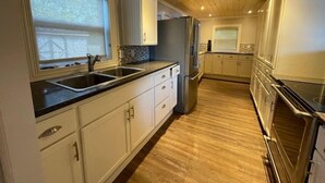 A modern kitchen with white cabinetry, a stainless steel refrigerator, and a wooden floor. - Bespoke Lake Cottage (Kings County)