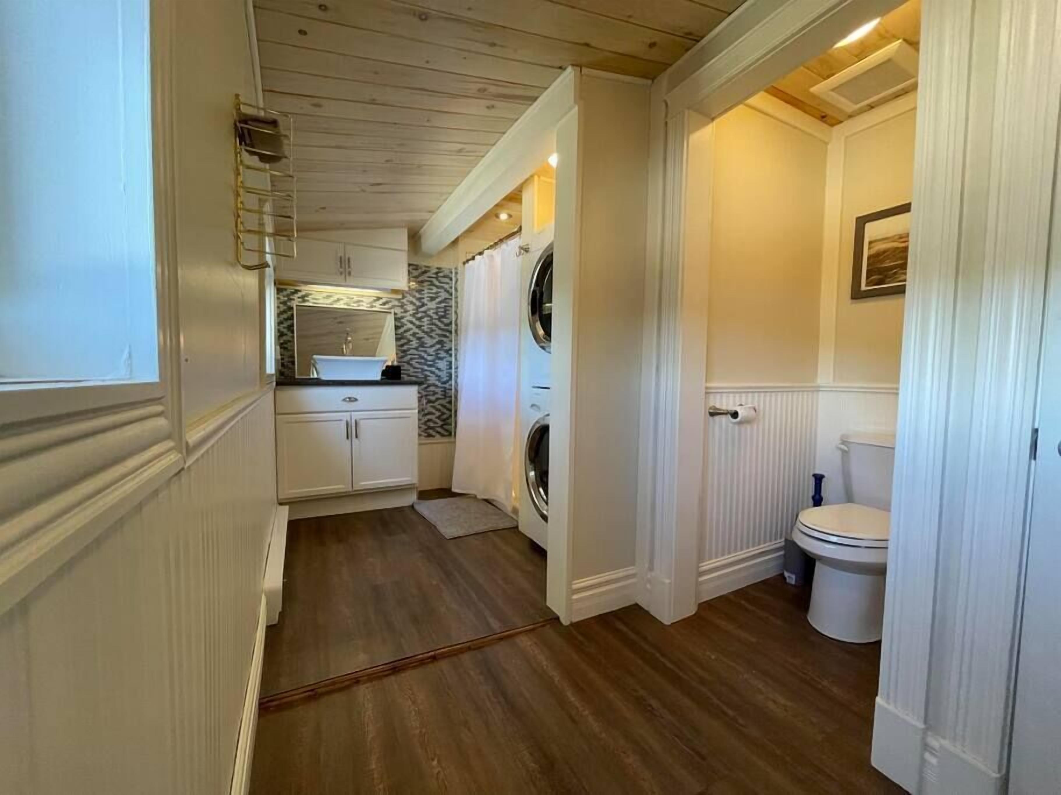 Un bagno moderno e funzionale, con pavimento in legno, un water, un lavandino con specchio e una lavatrice.