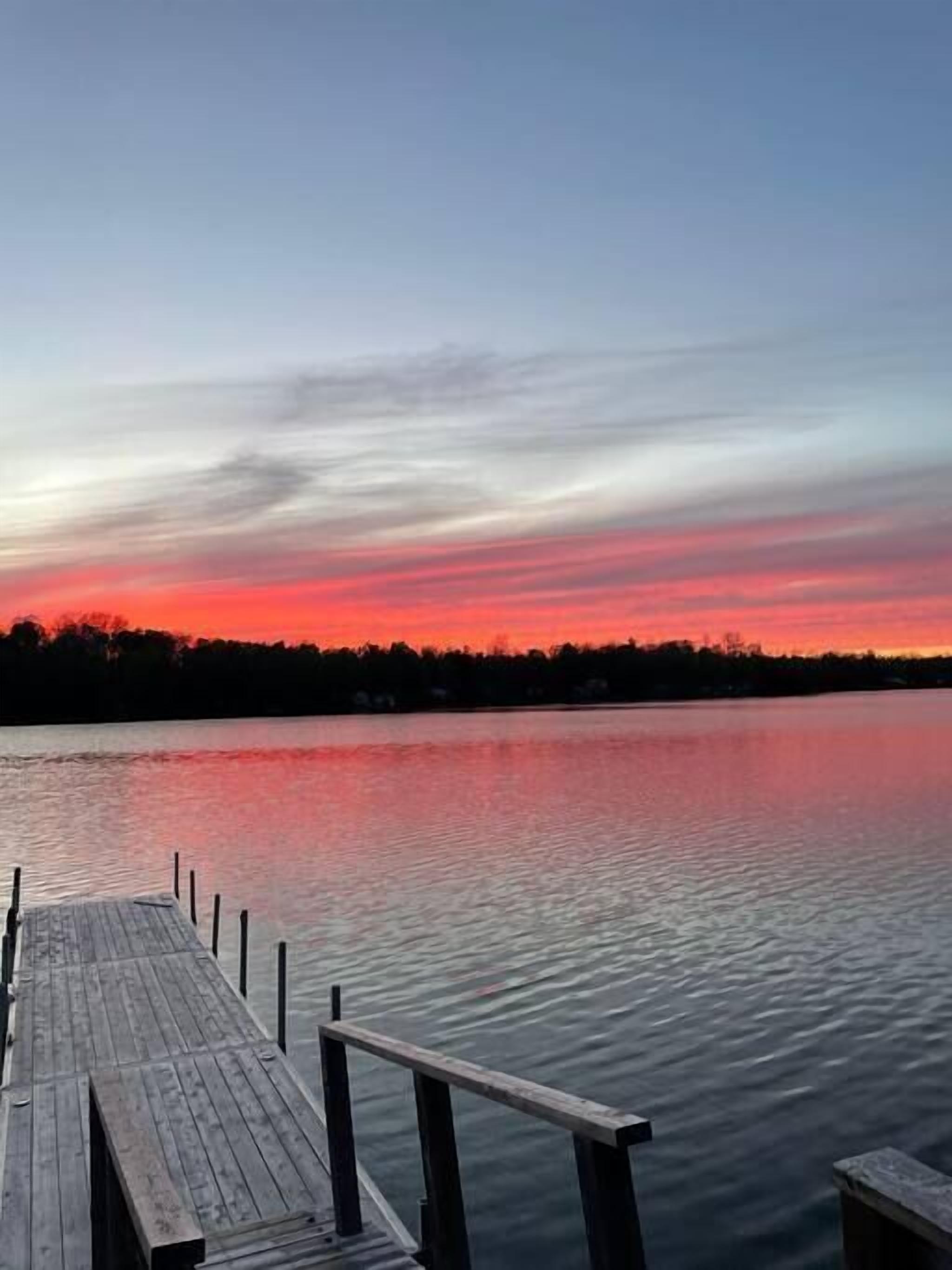 Eine Holzsteige führt in ruhiges Wasser, der Himmel färbt sich im Sonnenuntergang.