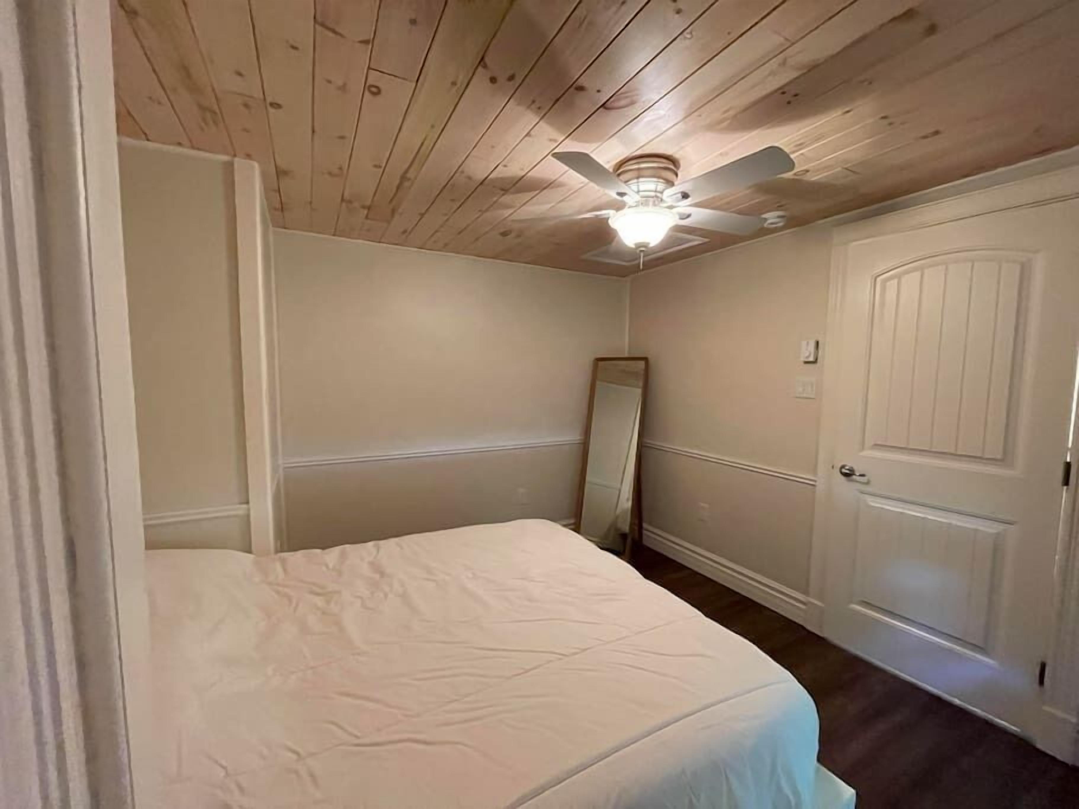 Ein Schlafzimmer mit Bett, Deckenventilator, Tür und Spiegel.