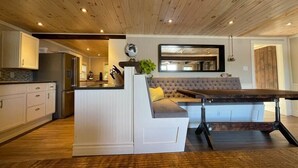 A modern kitchen with white cabinetry, a central island, and a dining area with a wooden table. - Bespoke Lake Cottage (Kings County)