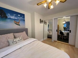 A bedroom with a bed, a painting of a boat on water, a ceiling light, and a view into a dining area. - Little Yellow House In The Heart Of The Valley 🏠 (Kings County)