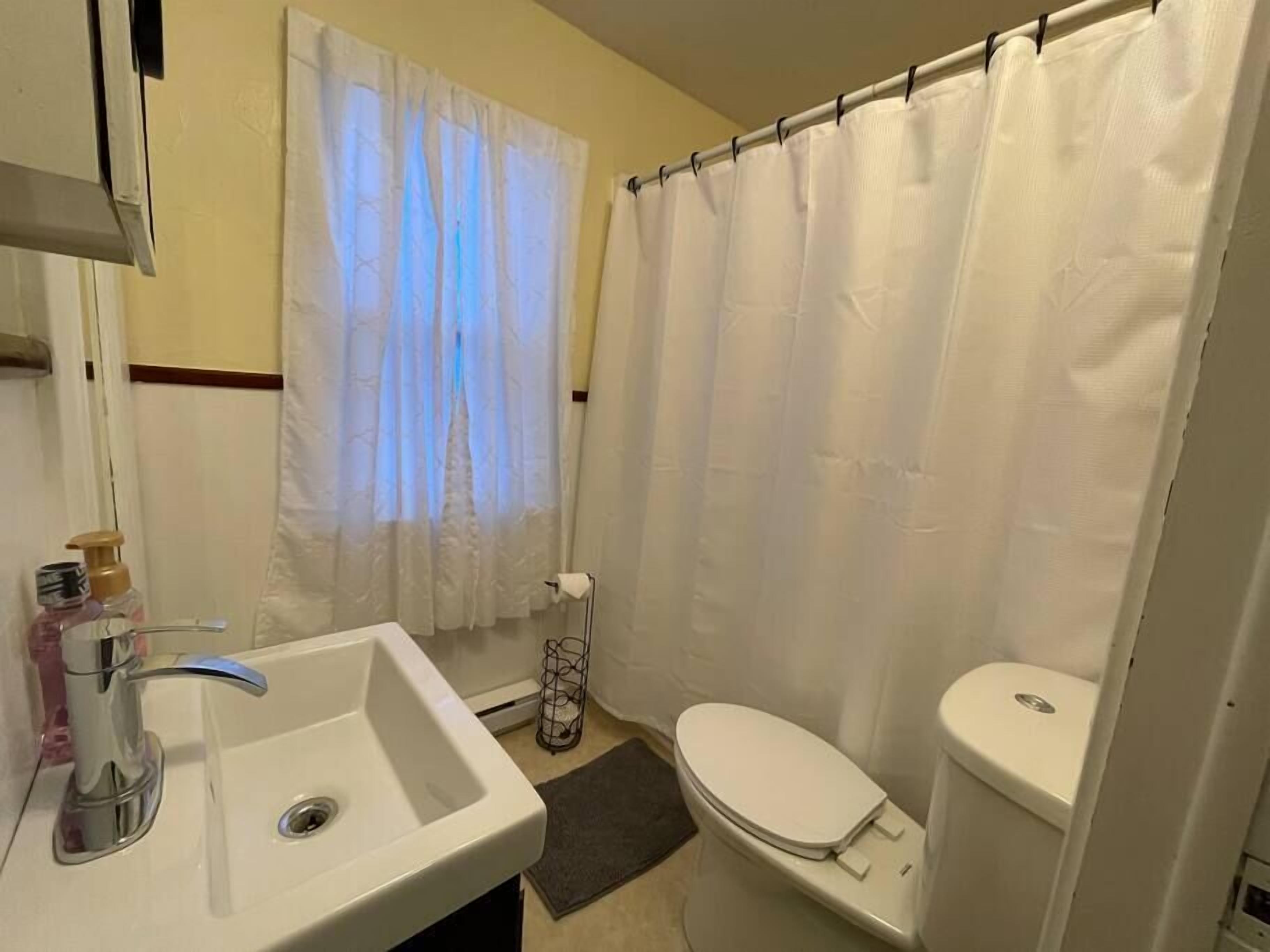 Un baño con lavamanos, inodoro y cortina de ducha blancos.