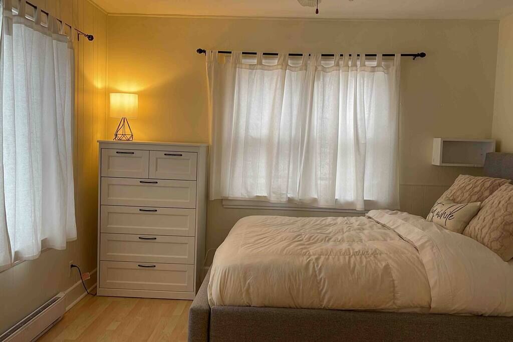 Un dormitorio con cama, cómoda, lámpara de noche y ventana con cortinas.