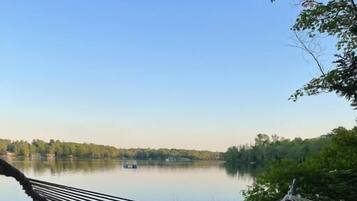 A hammock on a sandy beach overlooking a calm lake with trees and a boat in the distance.