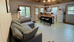 Un intérieur de chalet chaleureux avec un canapé, une table à manger, un coin cuisine et de grandes fenêtres.