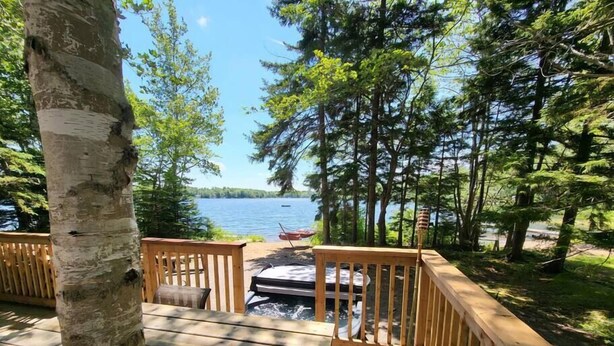 Une terrasse en bois avec un banc, donnant sur un lac entouré d’arbres.