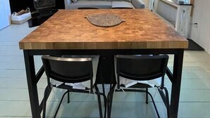 Une cuisine moderne avec une table en bois, des chaises noires, un canapé et un porte-casseroles suspendu.