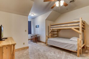 Ein Zimmer mit Etagenbett, Schreibtisch mit Stuhl, Deckenventilator und einem kleinen Tisch mit Hocker.