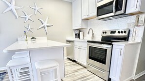 A modern kitchen with white cabinets, a built-in microwave, oven, and dishwasher. There are starfish decorations on the wall and a wooden floor. - Ocean View! Remodeled! Just Steps to the Beach, large pool and Bar. Gated resort (Hilton Head Island)