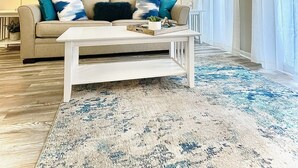 A living room with a beige sofa, a white coffee table, and a blue patterned rug. - Ocean View! Remodeled! Just Steps to the Beach, large pool and Bar. Gated resort (Hilton Head Island)