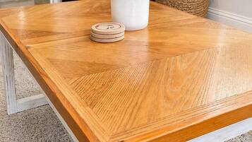 Une table de salle à manger en bois avec un piétement blanc, une tasse en céramique blanche et un sous-verre en bois.