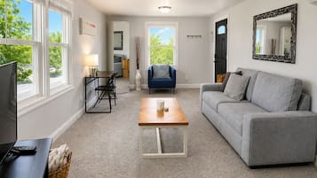 Un salon avec un canapé gris, une table basse en bois, un fauteuil bleu, un téléviseur et une cheminée.