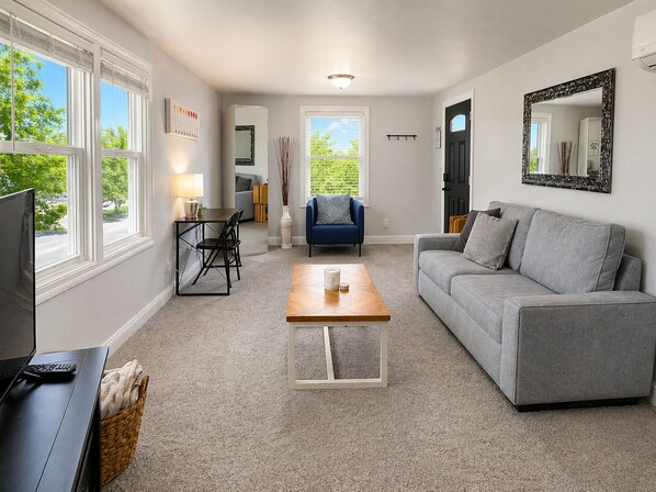 A living room with a grey sofa, a wooden coffee table, a blue armchair, a TV, and a fireplace.
