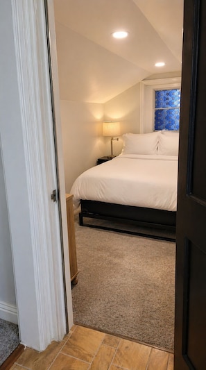 A bedroom with a bed, a nightstand, a lamp, a window with blue patterned glass, and a door. - Cozy Private Retreat Near Downtown + Hospital (Martinez)