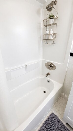 A white bathtub with a showerhead, a towel rack, and a shelf with toiletries.