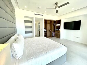 Quarto moderno com cama grande, ventoinha no teto, closet espaçoso e televisão na parede.