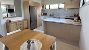 A modern kitchen with a central island, white cabinetry, and a dining area with a wooden table and white chairs. - Little Break Tahunanui - 5 minutes from beach (Nelson)