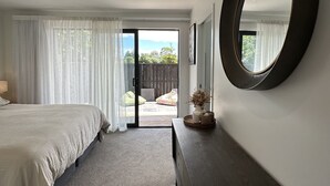 A bedroom with a large bed, a dresser, a mirror, and a view of the outdoors through a sliding door. - Little Break Tahunanui - 5 minutes from beach (Nelson)