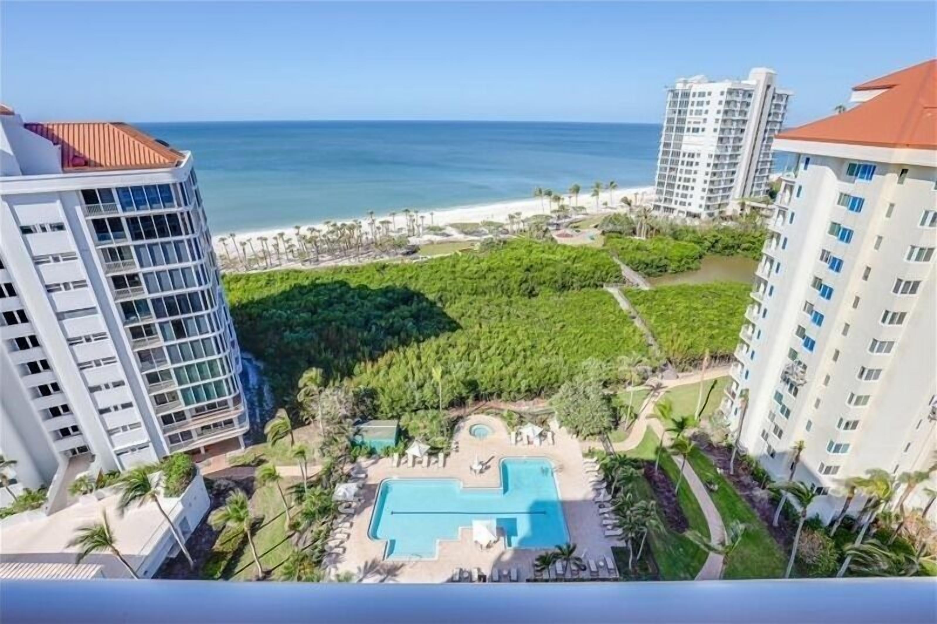 A hotel with a pool, surrounded by lush greenery and a view of the beach and ocean.