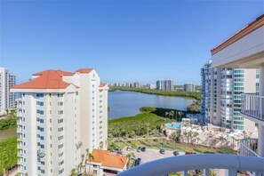 Un edificio de gran altura con techo rojo, vista a un lago y otros edificios residenciales al fondo.