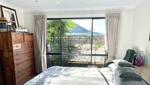 A bedroom with a large bed, wooden dresser, and a window with a view of greenery and a building.