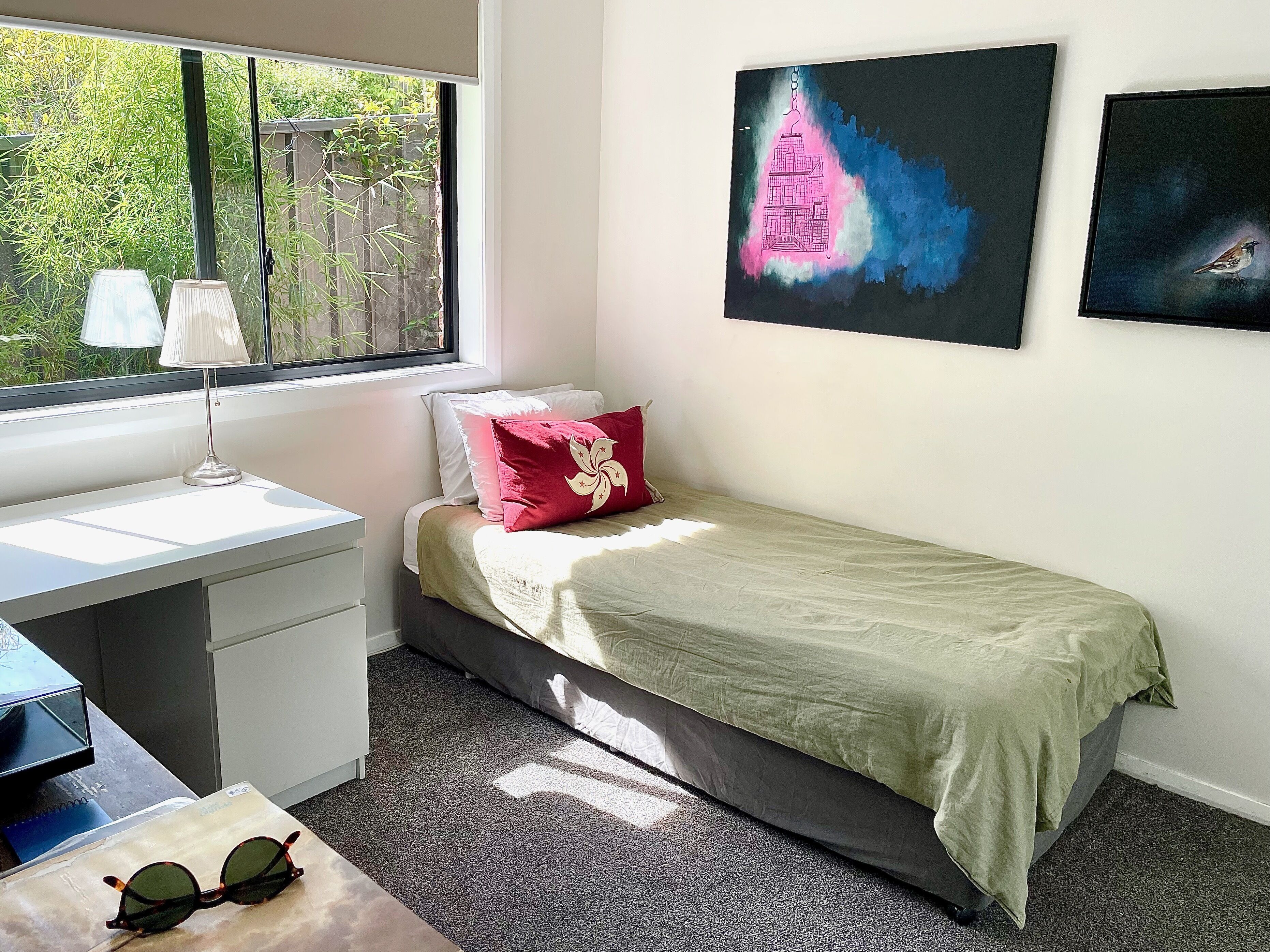Een slaapkamer met een bed, een bureau, een stoel, een raam en kunst aan de muur.
