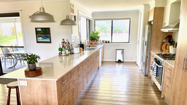 A modern kitchen with a central island, wooden cabinets, stainless steel appliances, and a large window providing natural light.