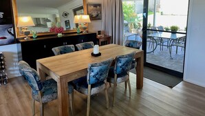 A dining area with a wooden table and blue upholstered chairs, a large mirror, and a view of an outdoor patio with a table and chairs.