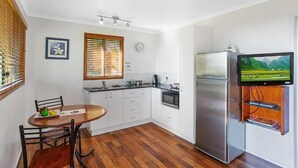 Une cuisine compacte comprenant un coin repas, un réfrigérateur, un four à micro-ondes et un téléviseur à écran plat fixé au mur.