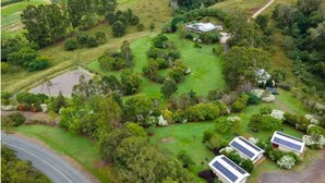 Vue aérienne d’une propriété comprenant une grande maison entourée d’une végétation luxuriante, un étang et des panneaux solaires sur le toit.