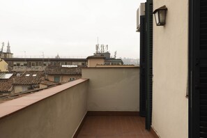 A narrow balcony with a tiled floor and a view of surrounding buildings.