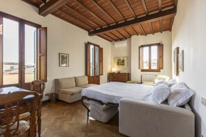 Un dormitorio con una cama, un sofá, una mesa de comedor de madera y una ventana.