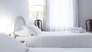 Une chambre d’hôtel avec deux lits, une table de chevet avec une lampe et une fenêtre avec des rideaux légers.