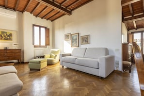 Amplia sala de estar con suelo de parqué, un sofá de color gris claro, un sillón amarillo y un mueble de madera.