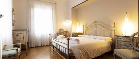 A bedroom with a wooden floor, a bed with white linens, two bedside tables with lamps, and a chair.