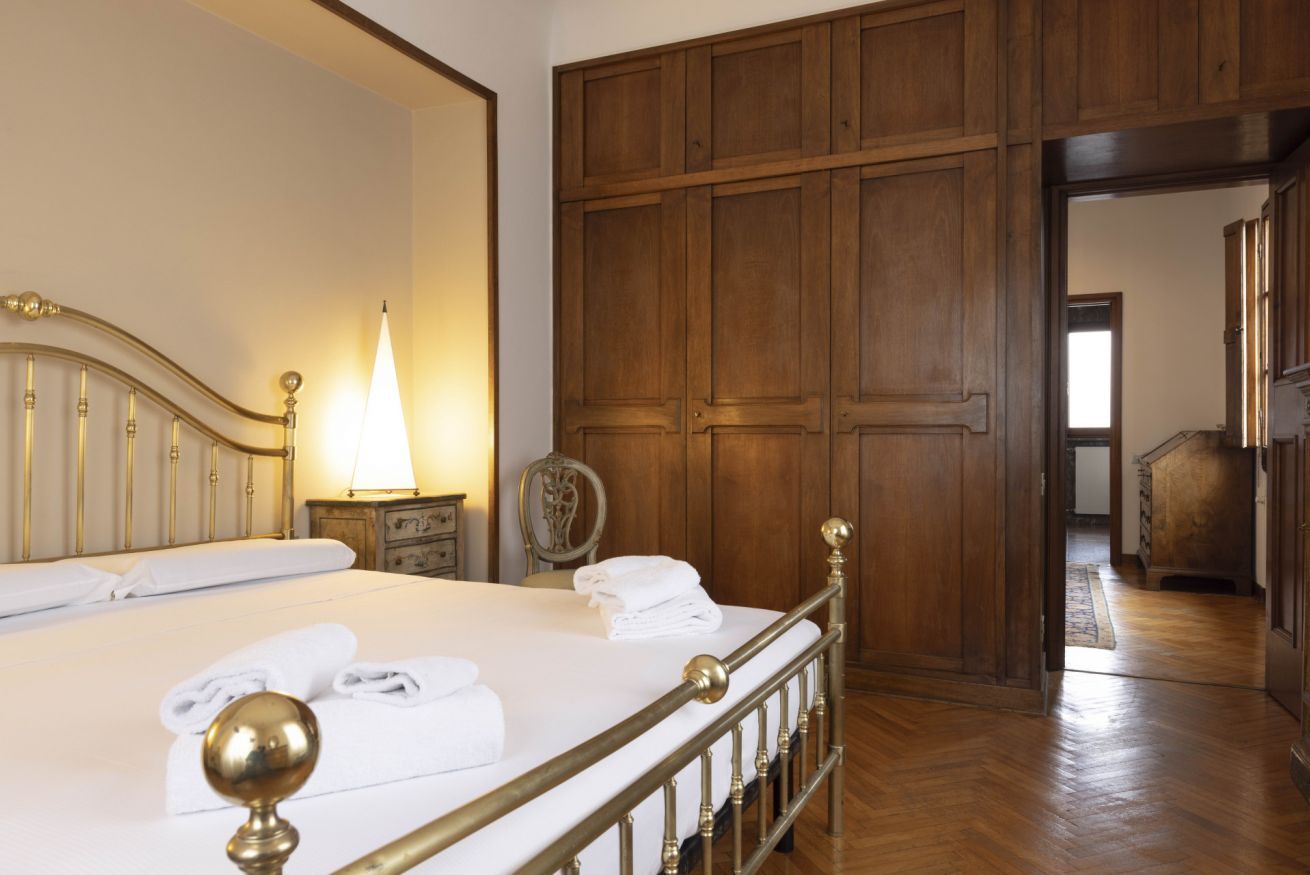 A hotel room with a bed, a nightstand with a lamp, and a wooden wardrobe.