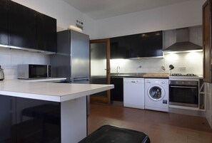 A modern kitchen with a central island, built-in appliances including a refrigerator, microwave, washing machine, and oven, and a separate sink area.