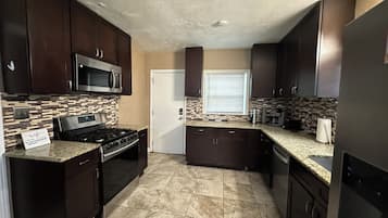 A kitchen with dark cabinets, a stainless steel microwave, a gas stove, and a tiled backsplash.